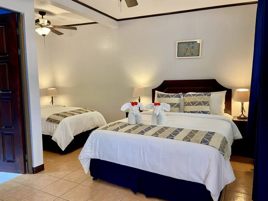 A hotel room with two beds, a ceiling fan, a nightstand with lamps, and a framed picture on the wall.