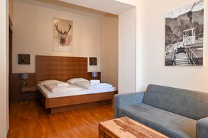 A modern hotel room with a wooden bed, a grey sofa, a wooden coffee table, and two wall-mounted lamps. - Post Residence Apartments 4B, incl SUMMER CARD (Zell am See)