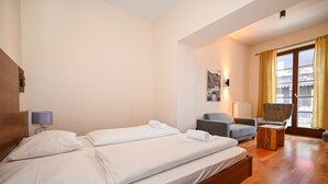 Hotellihuone, jossa on kaksi sänkyä, tuoli, pieni pöytä ja ikkuna, jossa on verhot.