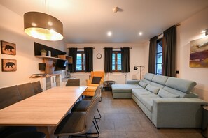 A modern living room with a dining area, a sofa, a TV, and a clock on the wall. - Post Residence Apartments 9A, sauna, SUMMER CARD (Zell am See)