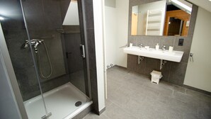 Een moderne badkamer met een douchecabine van glas, een witte wastafel en een grote spiegel.