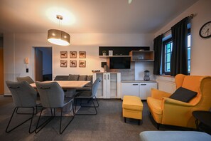 A modern kitchen with a dining area, a TV, and a window with curtains.