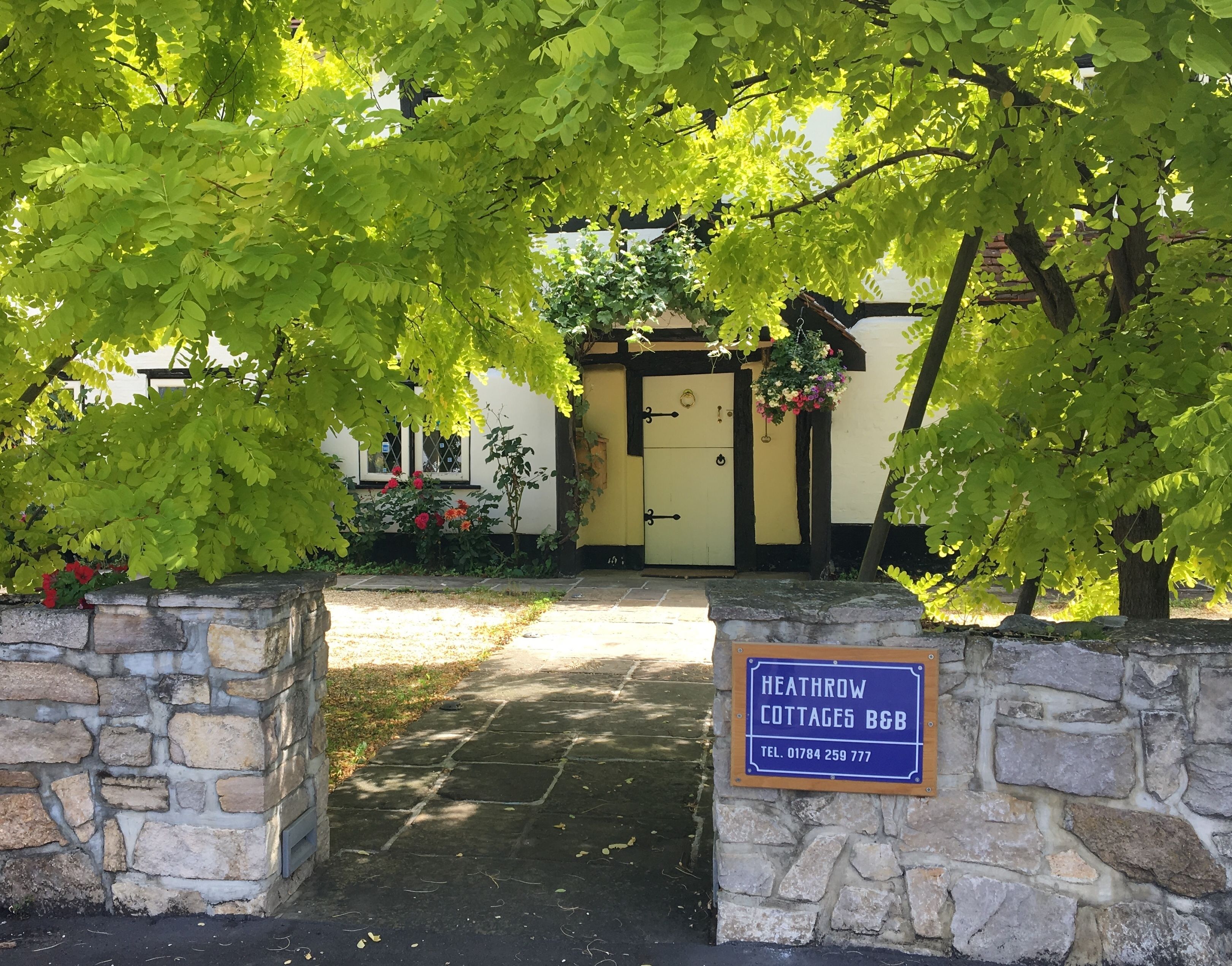A stone wall entrance to a property named 'Heathrow Cottages B&B' with a stone pathway leading to a yellow door.
