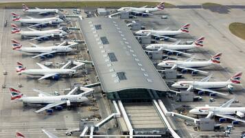 An airport terminal with multiple British Airways planes parked at gates, connected to jet bridges.