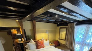 Un dormitorio acogedor con una cama grande, un cabecero de madera, una mesita de noche, una lámpara y una ventana con cortinas.