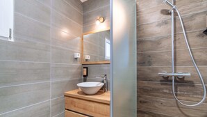 Un baño con tocador de madera, un espejo grande y una ducha moderna.