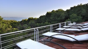 A row of sunbeds with white cushions on a terrace overlooking a body of water and a forested hillside. - Dimora Villa Serena Porto Selvaggio (Nardò)
