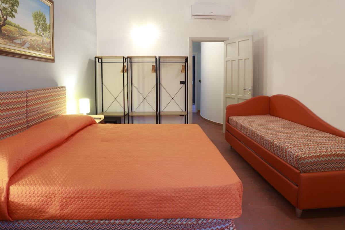 Une chambre avec un grand lit et un petit canapé, un tableau au mur et une armoire avec des miroirs.