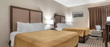 A hotel room with two beds, each with a headboard, bedside lamps, and a small table with a chair.
