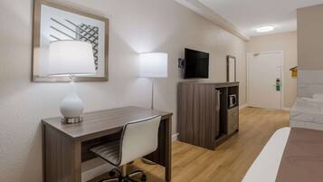 A hotel room with a wooden desk, a chair, a television, a minibar, and a bed.