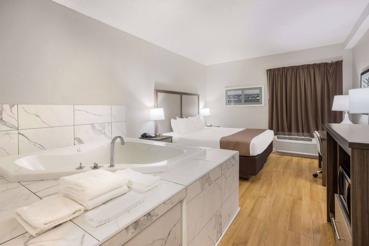 Habitación de hotel con baño amplio, dos camas, escritorio y televisor.