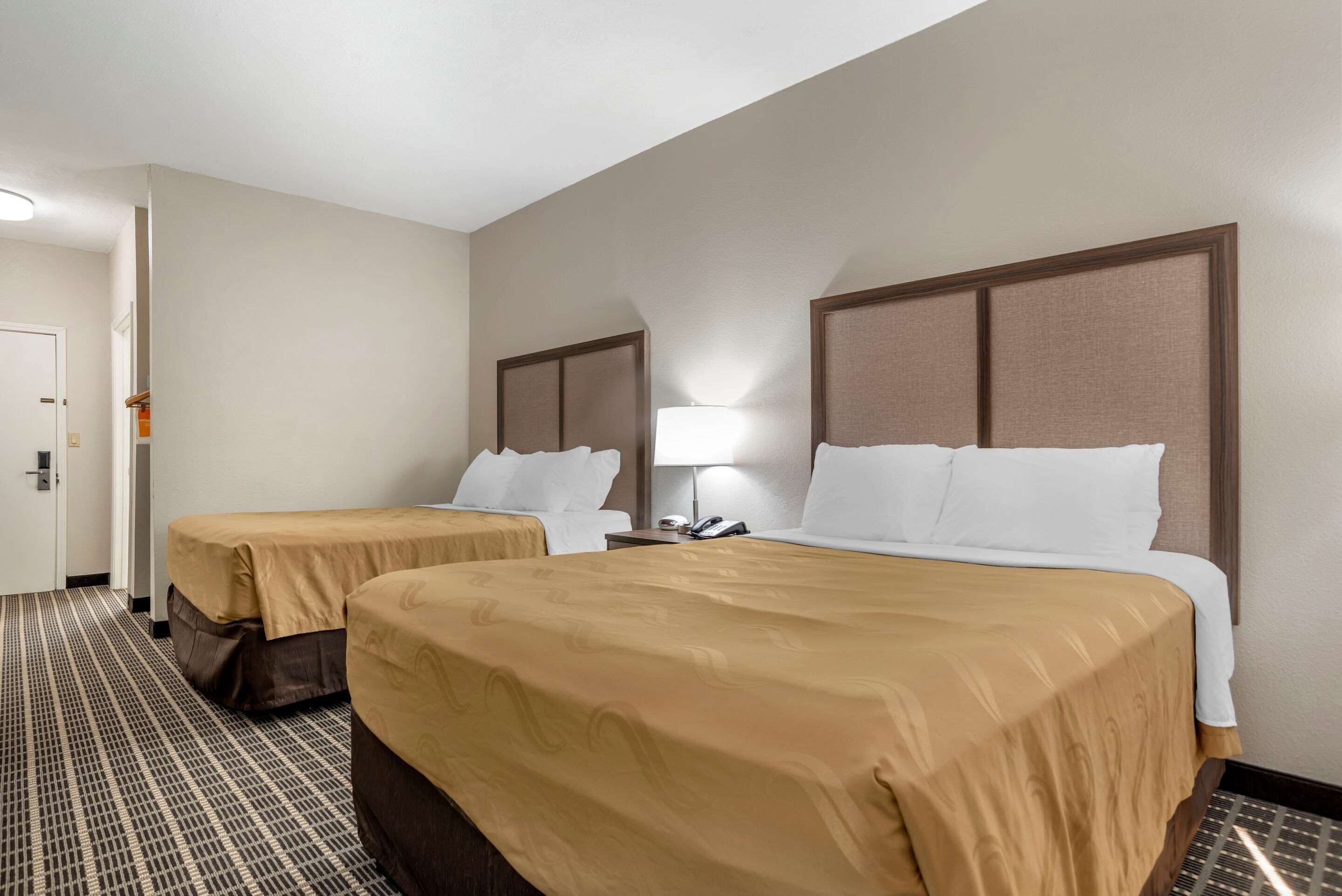 Ein Hotelzimmer mit zwei Betten, einem Nachttisch mit Lampe und einem gemusterten Teppich.