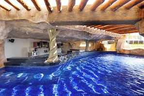 Una piscina con un diseño singular, zona de bar y techo rústico de piedra.