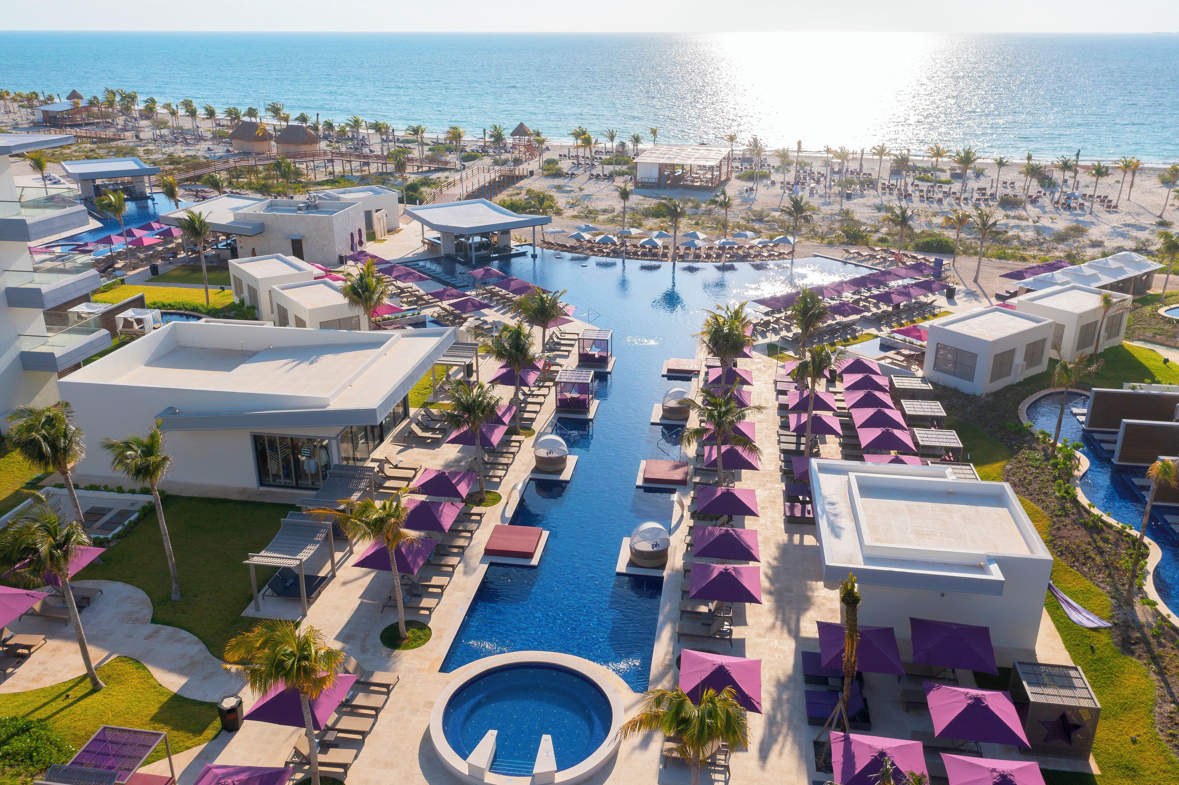 A resort with a central pool, multiple lounge areas, and a beach view.