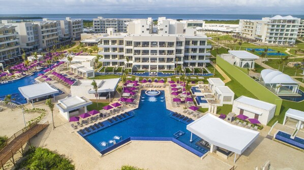 Un complejo turístico con varias piscinas, una fuente central y un gran edificio con balcones.
