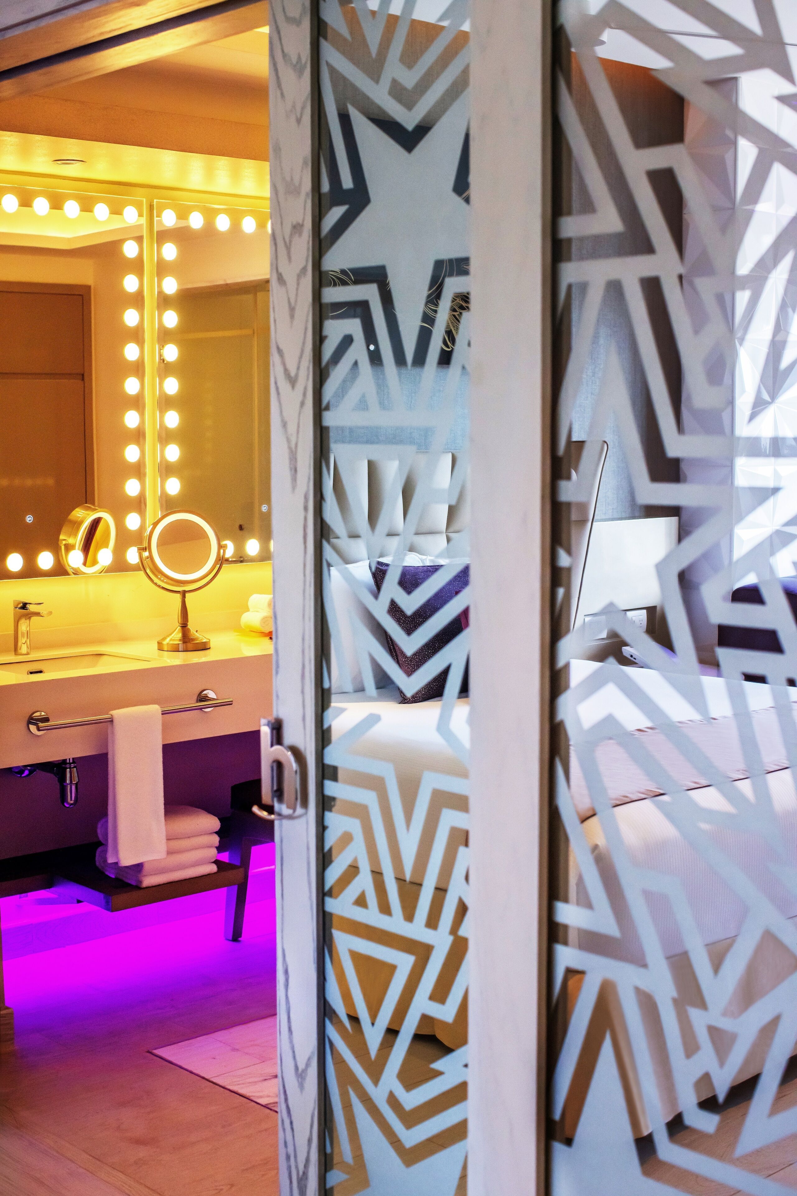 Une salle de bain avec un meuble-lavabo, un miroir avec éclairage intégré, un porte-serviettes et un lambris mural à motifs.