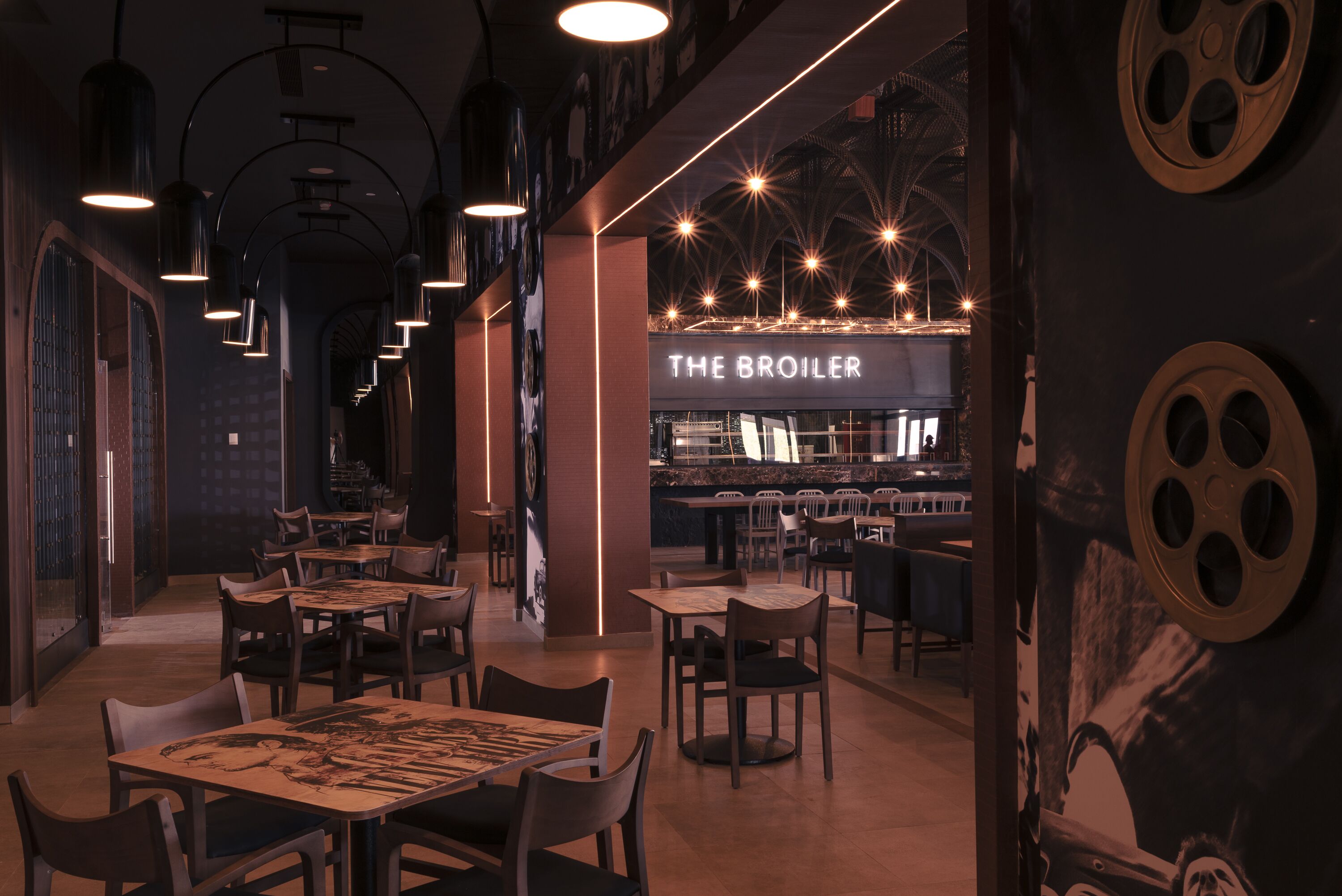 Ein Restaurantinneres mit Tischen und Stühlen, einer Bar und einem leuchtenden Neonzeichen mit der Aufschrift 'THE BROILER'.