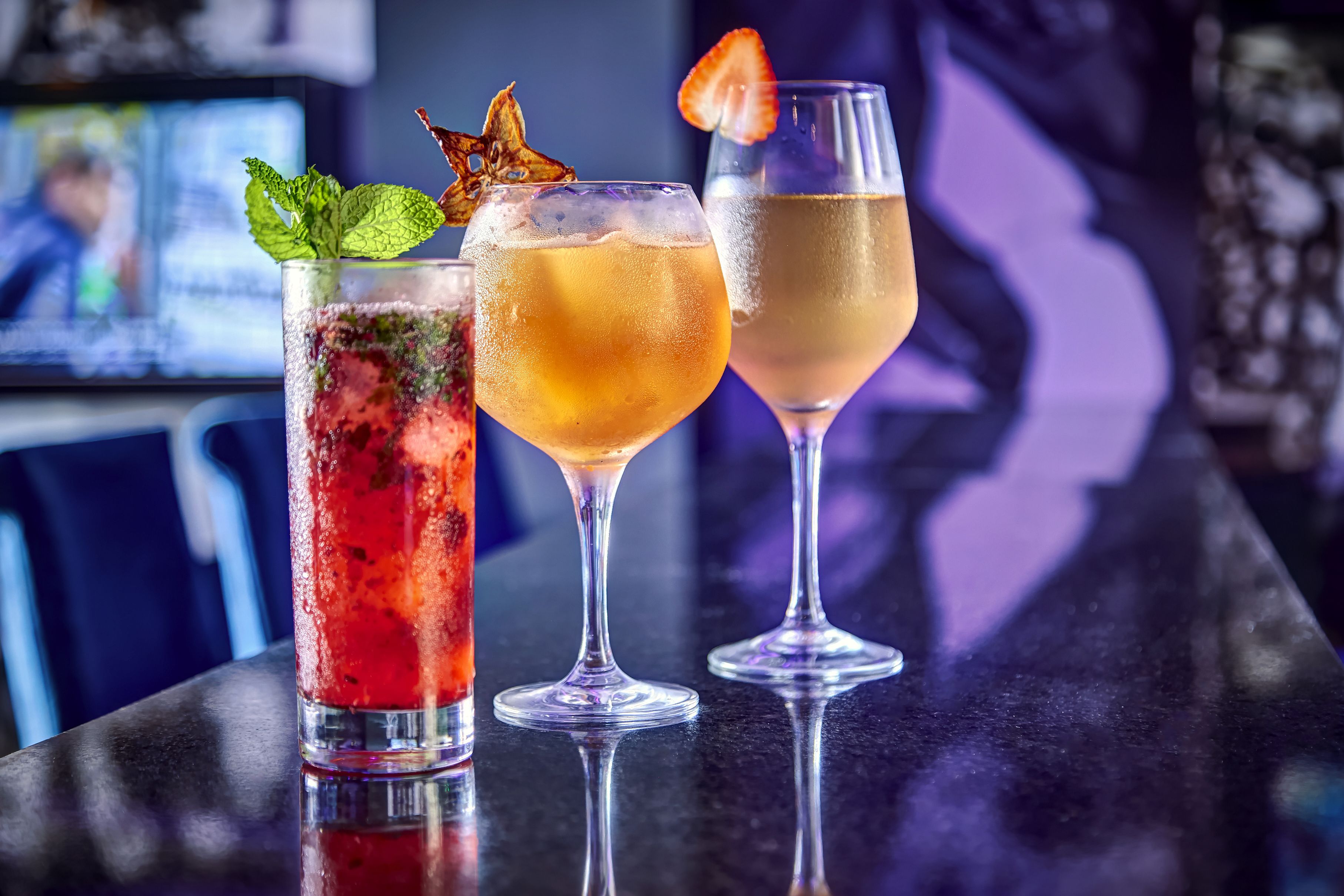 Three cocktails on a bar counter with a blurred background.