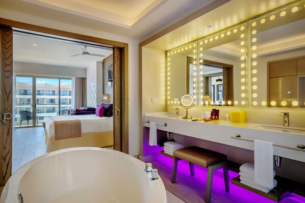 A hotel room with a large bed, a bathroom with a vanity, a bathtub, and a balcony with a view of the hotel buildings. - Planet Hollywood Cancun Adult Scene by Royalton, An Autograph Collection® All-Inclusive Resort - Adults Only (Costa Mujeres)