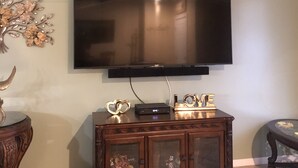 Un salon doté d’un téléviseur à écran plat fixé au mur, d’un meuble en bois en dessous et d’un ventilateur de plafond.