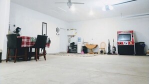 Une pièce spacieuse avec une table et des chaises, un ventilateur de plafond, une petite table avec un bol, et une machine rouge sur la droite.