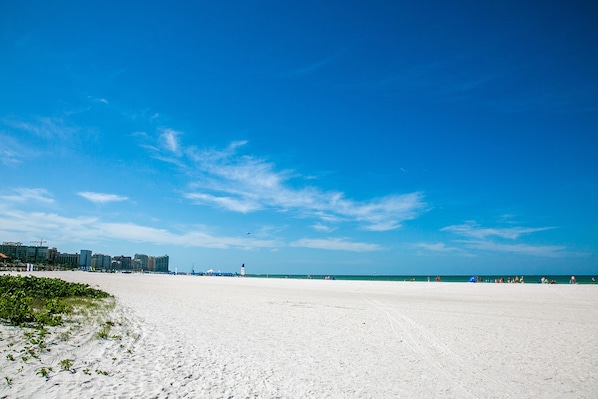A wide sandy beach with a clear blue sky and distant buildings.