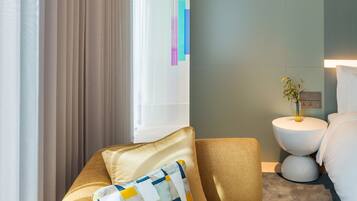 A modern hotel room with a sofa, a bedside table with a vase, and a wall-mounted light.