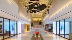 Un vestíbulo de hotel moderno con una escalera central, paredes de vidrio y una escultura decorativa.