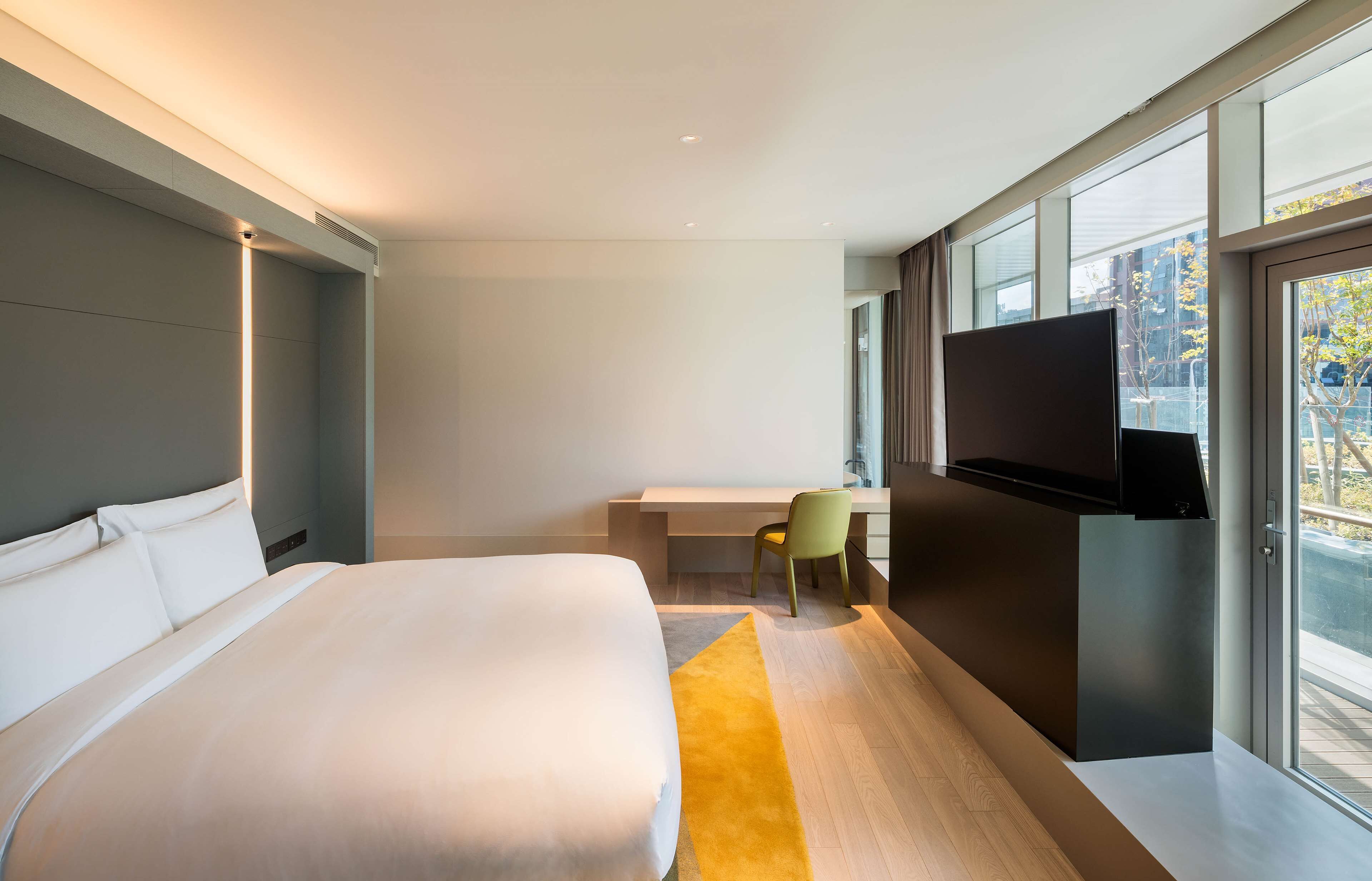 Ein modernes Hotelzimmer mit einem großen Bett, einem Schreibtisch, einem Sessel und einem Fernseher.