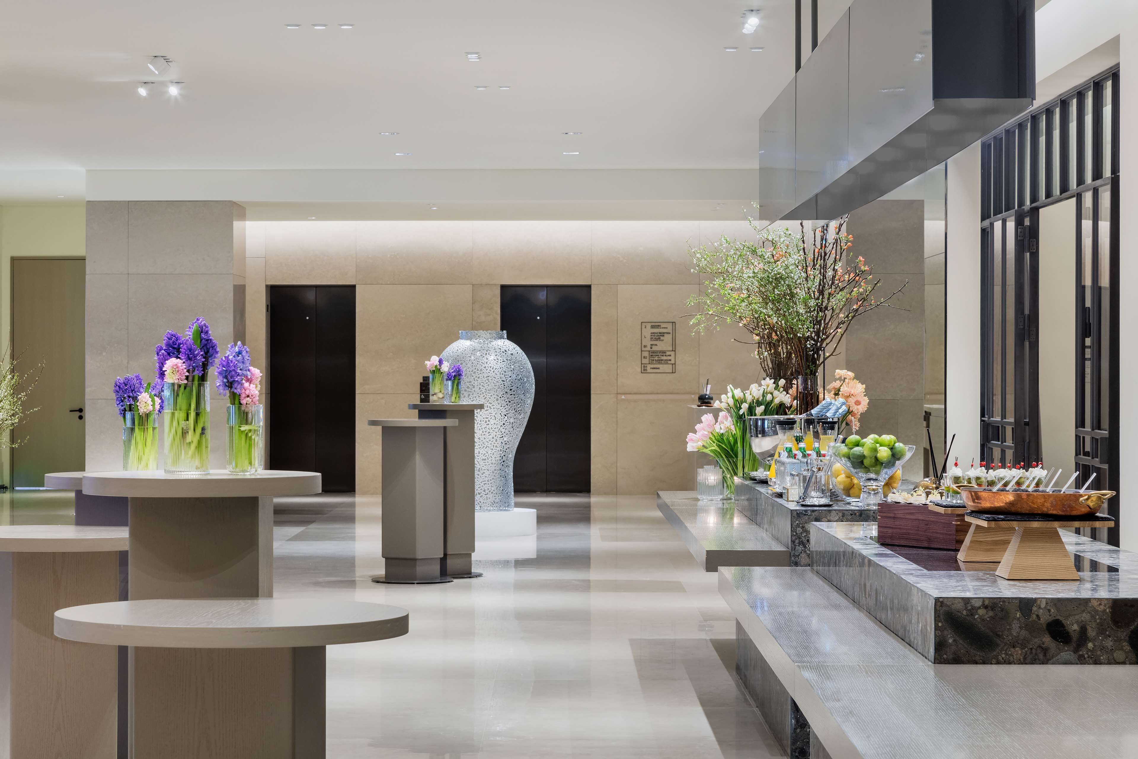 Un vestíbulo moderno con una recepción, una escultura de vidrio decorativa y una zona de buffet con diversas opciones de comida.