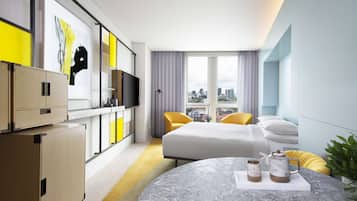 A modern hotel room with a bed, a round table with a coffee set, a TV, and a city view.