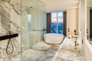 A modern bathroom with a large bathtub, a glass shower enclosure, and a city view.