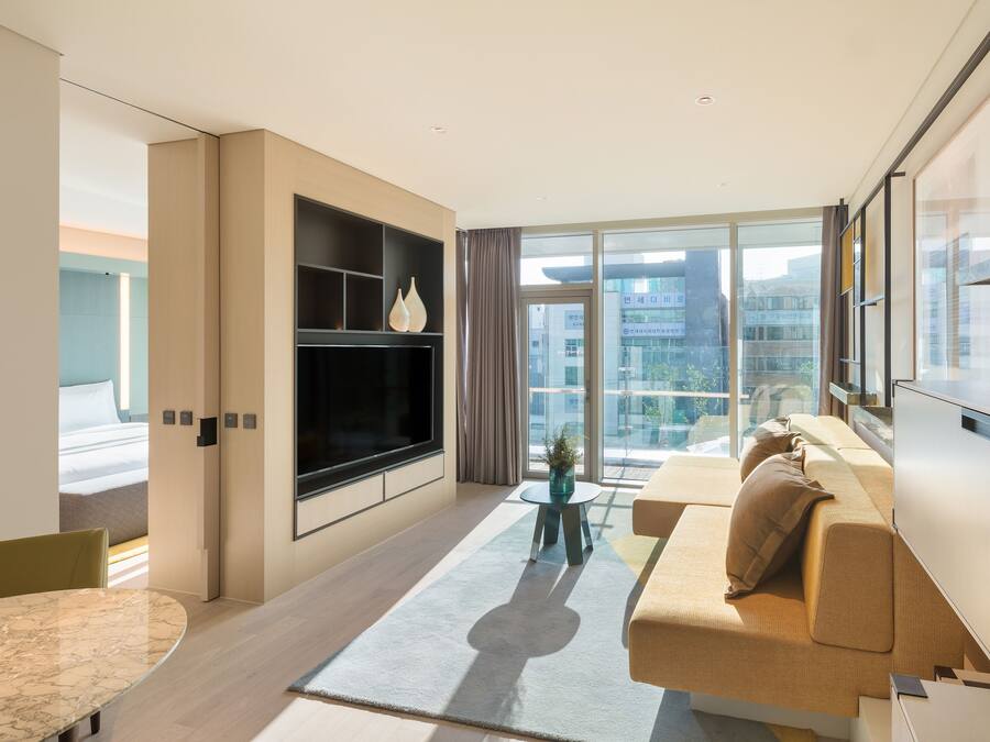 A modern hotel room with a large bed, a sofa, a TV, and a view of the city.