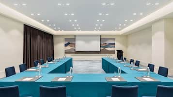 A conference room with a long table, blue chairs, and a projector screen.