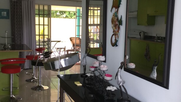 A dining area with a bar, red bar stools, and a table with magazines. There are chairs and a large mirror on the wall. - Best Villas Tobago (Lowlands)