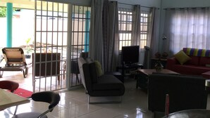 A spacious living area with a sofa, TV, and a dining table with chairs. - Best Villas Tobago (Lowlands)