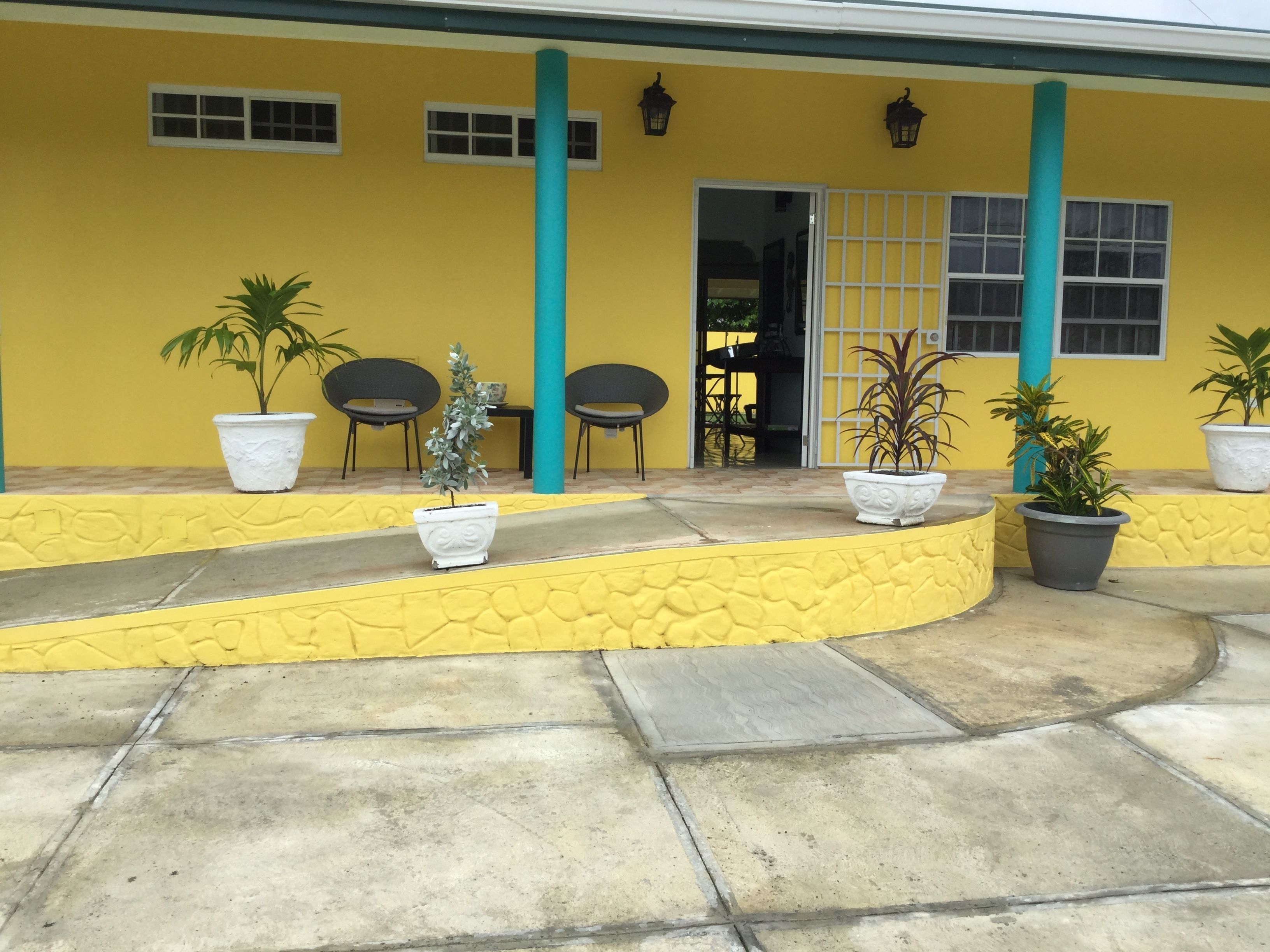 A yellow building with a covered patio area, potted plants, and outdoor seating.