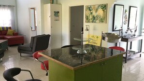 A hotel room with a green desk, a red chair, a black chair, a red sofa, a white wardrobe, a mirror, and a painting on the wall. - Best Villas Tobago (Lowlands)