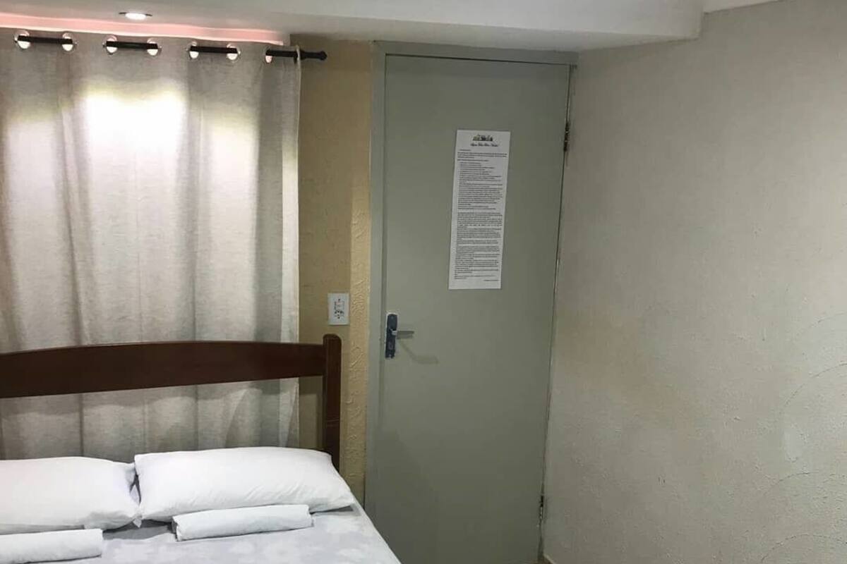 A hotel room with a bed, a door with a notice, and a curtain.