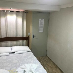 A hotel room with a bed, a door with a notice, and a curtain.