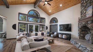 A spacious living room with a large sectional sofa, a stone fireplace, and a flat-screen TV mounted on the wall. - Paradise Awaits - Updated Donner Lake Home, Private Hot Tub, Dog Friendly, BBQ and Big Deck (Truckee)