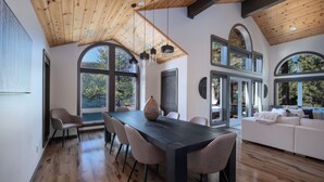 A modern interior with a wooden ceiling, large arched windows, a dining area with a black table and chairs, and a white sofa. - Paradise Awaits - Updated Donner Lake Home, Private Hot Tub, Dog Friendly, BBQ and Big Deck (Truckee)