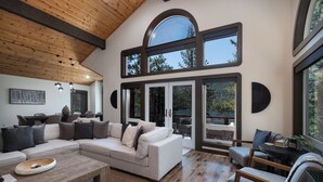 A spacious living room with a large sectional sofa, a wooden coffee table, and a dining area with a round table and chairs. - Paradise Awaits - Updated Donner Lake Home, Private Hot Tub, Dog Friendly, BBQ and Big Deck (Truckee)
