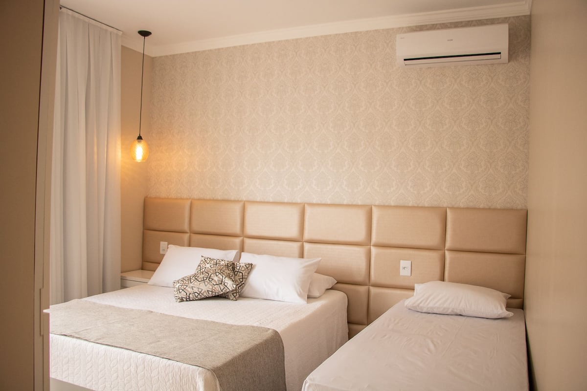 Habitación de hotel con dos camas, un papel tapiz estampado, aire acondicionado y una lámpara de noche.