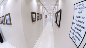 Un pasillo de hotel con cuadros enmarcados en las paredes, un cartel con texto y un suelo limpio de baldosas.