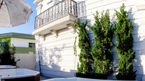 Zona de piscina con un edificio blanco, un balcón y vegetación.