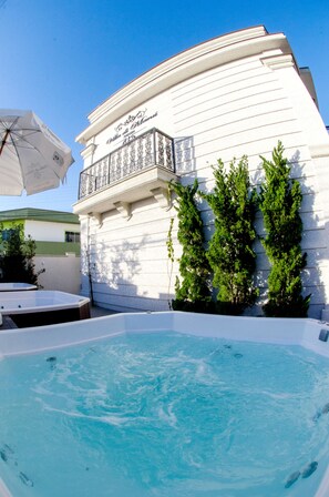 A swimming pool area with a white building, a balcony, and greenery. - Pousada Villa di Manú (Penha)