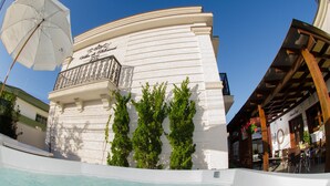 Un edificio con fachada blanca, un balcón con barandilla y una piscina al frente.