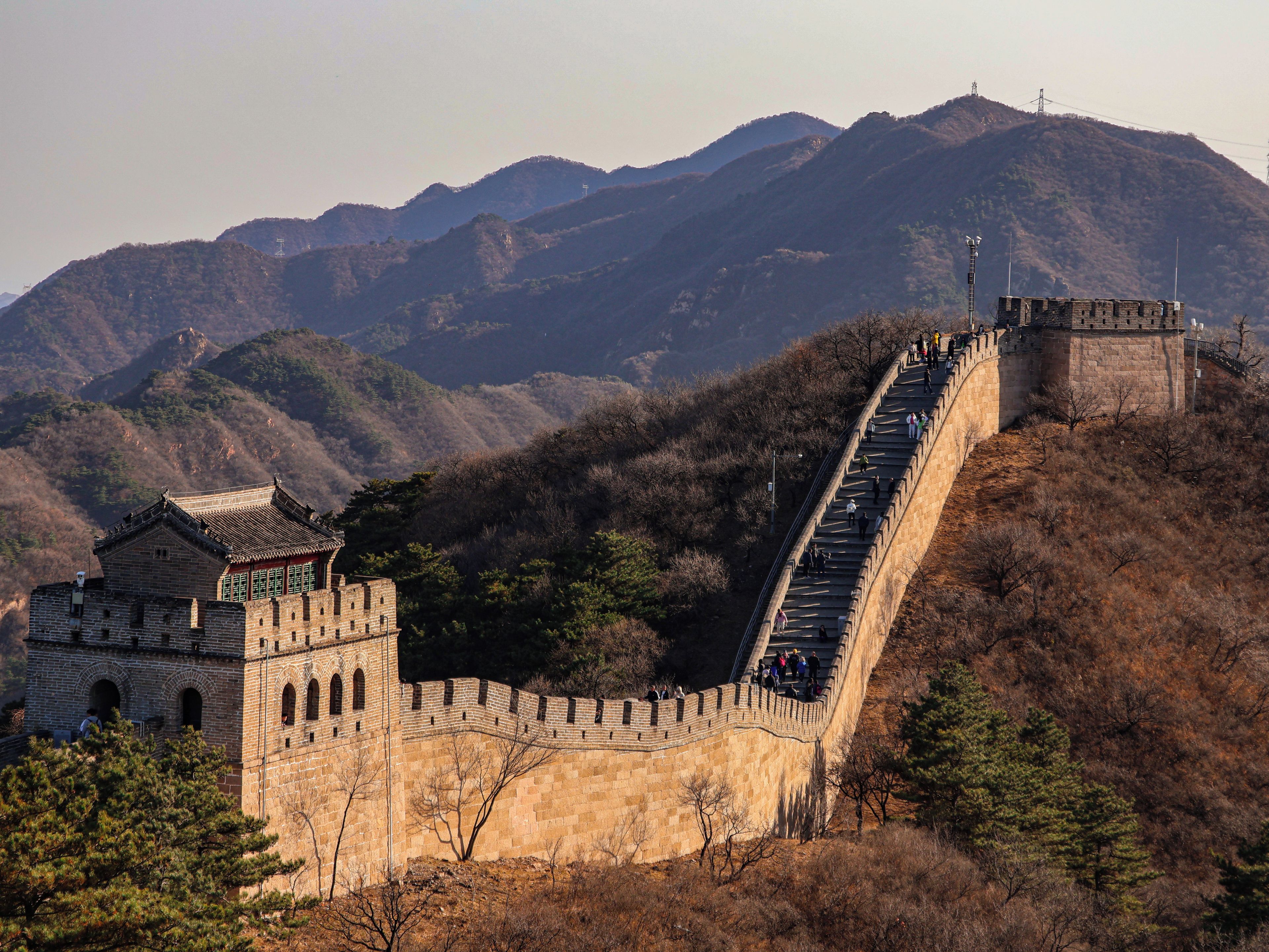 A stone wall with a traditional building at the base, surrounded by mountains.