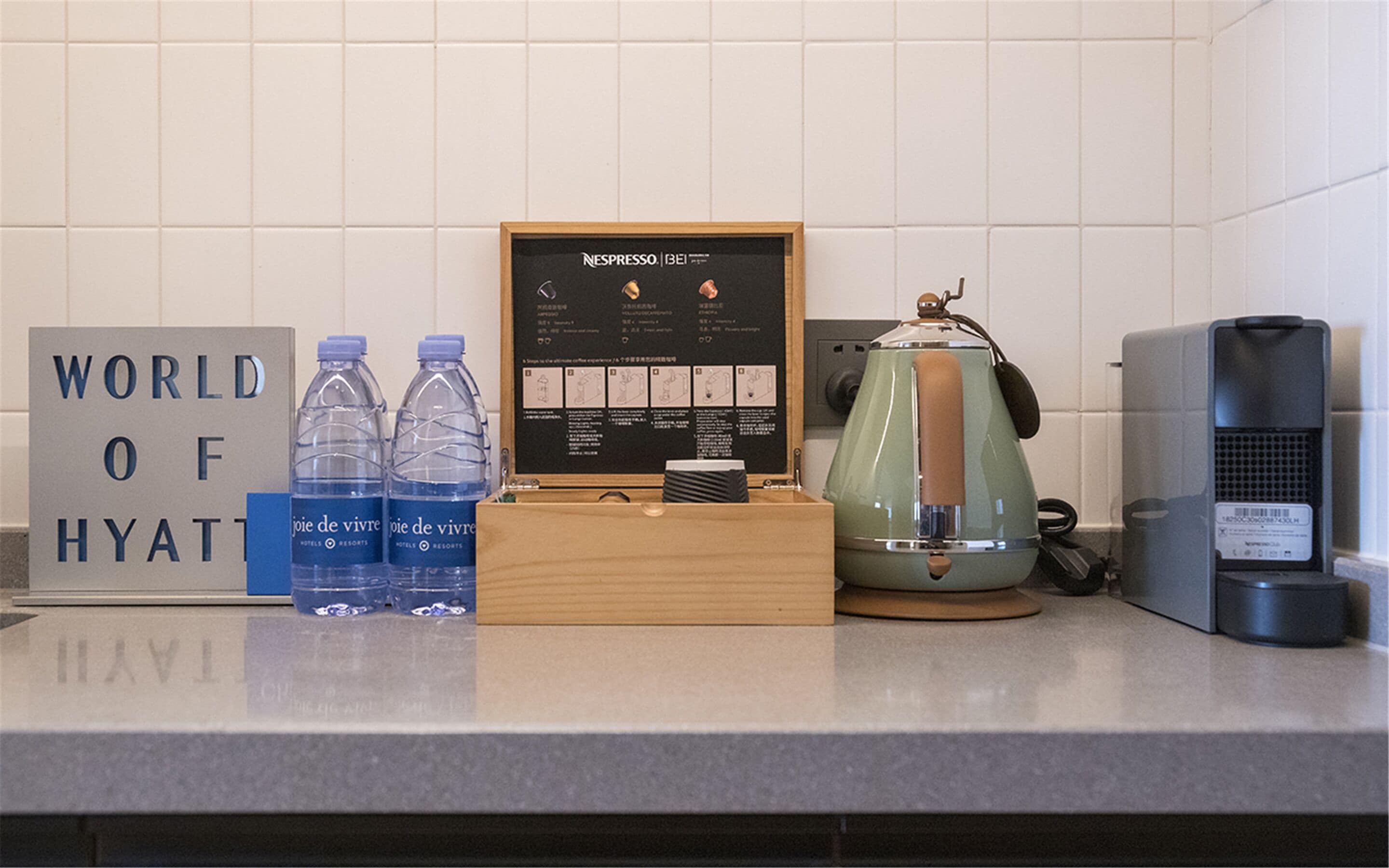 A kitchen counter with a coffee maker, a framed menu, bottled water, and a sign reading "WORLD OF HYATT".